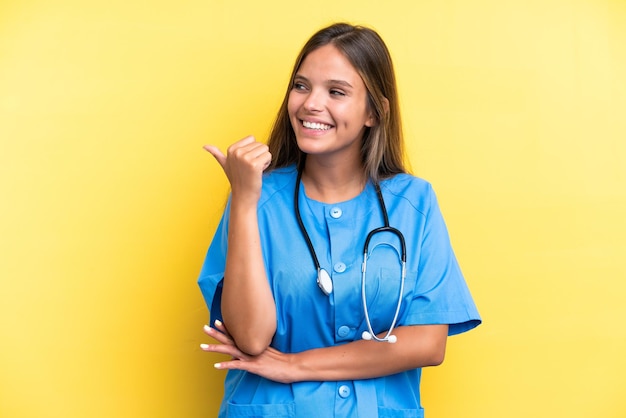 Kaukasische frau der jungen krankenschwester lokalisiert auf gelbem hintergrund, der auf die seite zeigt, um ein produkt zu präsentieren