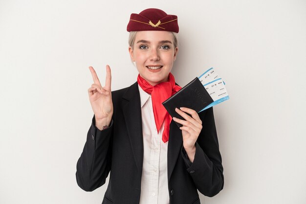 Kaukasische Frau der jungen Stewardess, die den Reisepass lokalisiert auf weißem Hintergrund hält, freudig und sorglos, der ein Friedenssymbol mit den Fingern zeigt.
