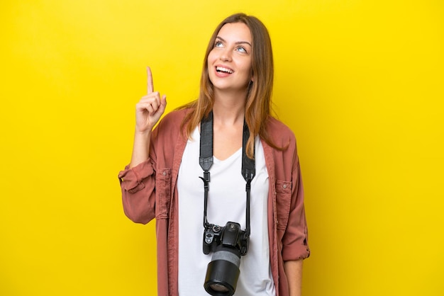 Kaukasische frau des jungen fotografen lokalisiert auf gelbem hintergrund, der nach oben zeigt und überrascht