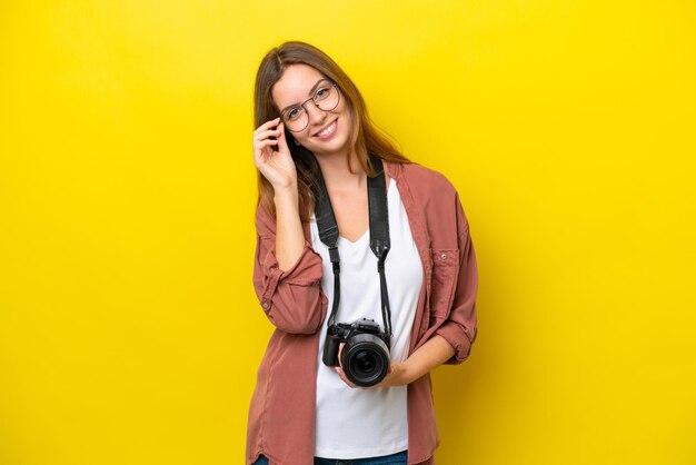 Kaukasische Frau des jungen Fotografen lokalisiert auf gelbem Hintergrund mit Gläsern und glücklich