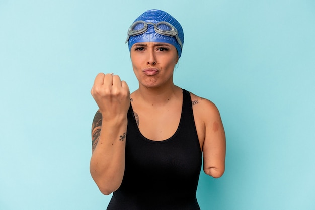 Kaukasische Frau des jungen Schwimmers mit einem Arm lokalisiert auf blauem Hintergrund, der Faust zur Kamera zeigt, aggressiver Gesichtsausdruck.
