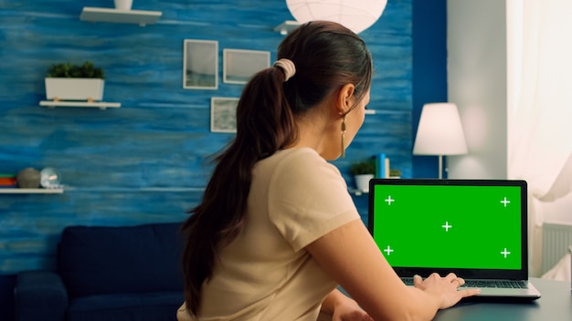 Kaukasische Frau, die an Laptop-Computer mit Mock-up-Chroma-Key-Display für den grünen Bildschirm für das persönliche Geschäft arbeitet