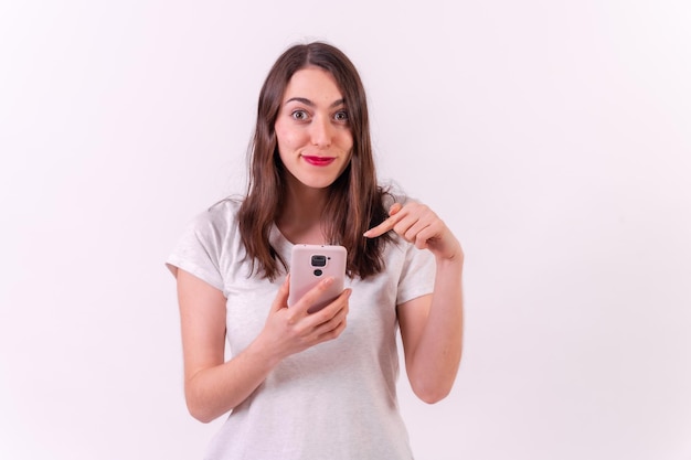 Kaukasische Frau, die auf ein Telefon zeigt, das auf einem weißen Hintergrundtechnologiekonzept lokalisiert wird