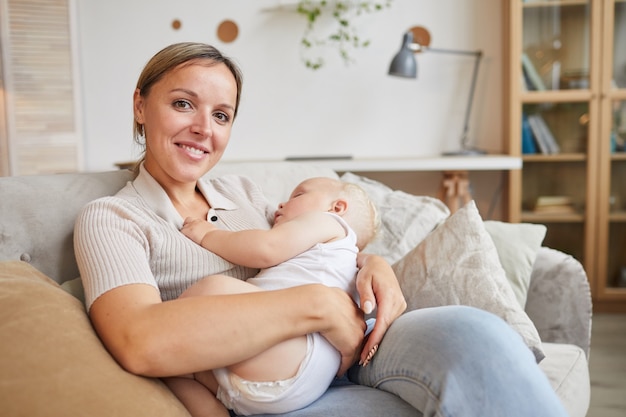 Kaukasische Frau, die auf Sofa sitzt und ihren schönen kleinen Sohn in den Armen kuschelt