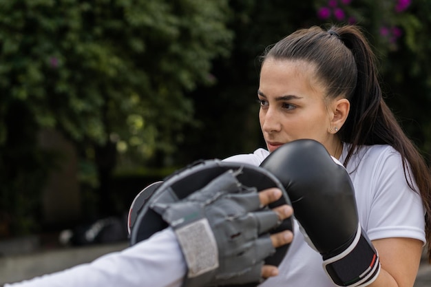 Kaukasische Frau, die einen Fäustling mit Boxhandschuhen schlägt, trainiert im Freien. Gesunder Lebensstil.