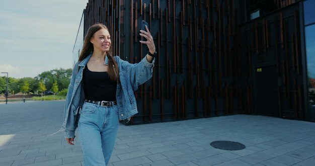 Kaukasische Frau, die ihr Smartphone für den Videoanruf verwendet, während sie auf der Straße spazieren geht Frau mit Videoanruf auf dem Handy beim Stadtspaziergang