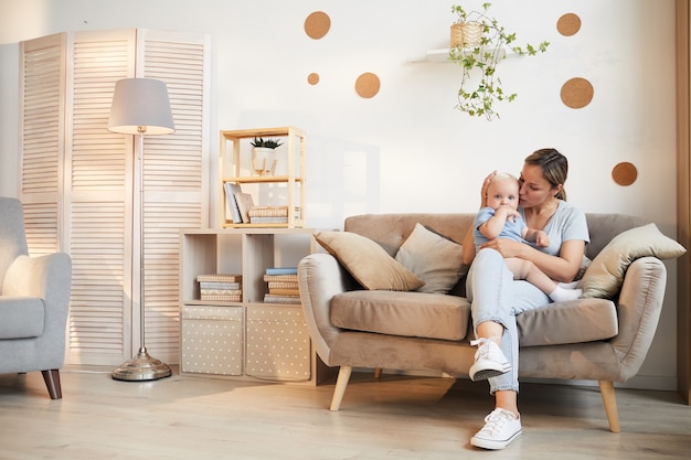 Kaukasische Frau, die lässiges Outfit trägt, das auf Sofa mit ihrem Kind auf Schoß sitzt