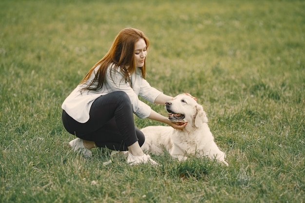 Kaukasische Frau, die mit ihrem Hund auf einem Gras sitzt. Mädchen mit weißer Jacke und Jeans