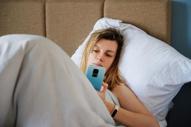 Kaukasische Frau, die sich im Bett entspannt und Smartphone benutzt