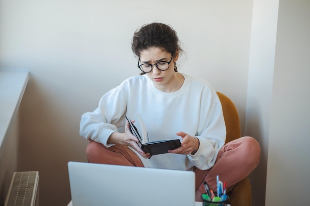 Kaukasische Frau, die zu Hause mit Brille arbeitet und Laptop-Lesebuch verwendet, flexibles Arbeiten für ...