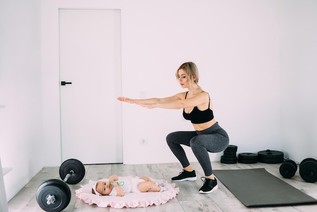 Kaukasische Frau hockt und macht Fitness zu Hause mit einem kleinen Kind Das Konzept der körperlichen Aktivität nach der Geburt