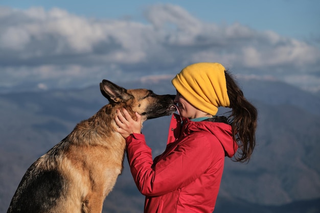 Kaukasische Frau in roter Jacke steht auf dem Berg neben ihrem Hund und genießt die Landschaft bei Sonnenuntergang