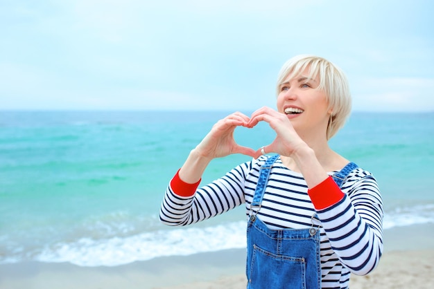 Kaukasische Frau mit Händen als Liebeszeichen im Urlaub am Meer