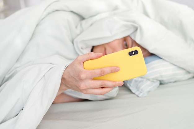 Kaukasische Frau mit Handy im Bett