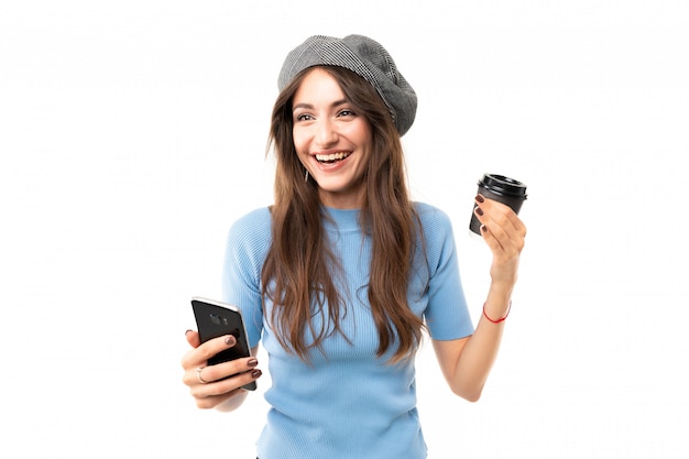 Kaukasische Frau mit Kappe trinkt Kaffee und lächelt, Bild lokalisiert auf weißem Hintergrund