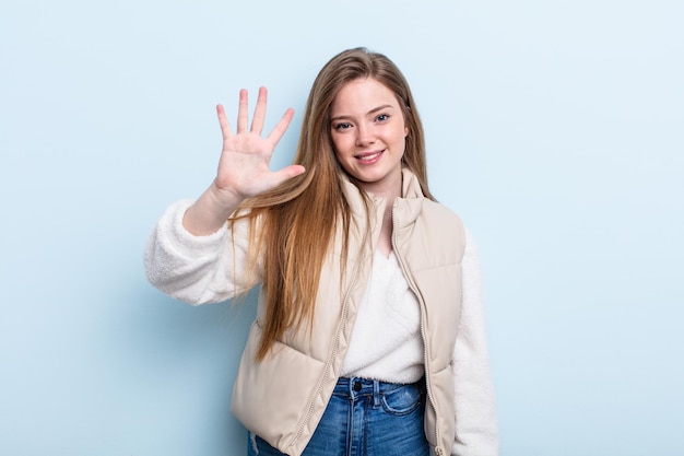 Kaukasische Frau mit roten Haaren, die lächelt und freundlich aussieht, Nummer fünf oder fünf mit der Hand nach vorne zeigend, rückwärts zählend