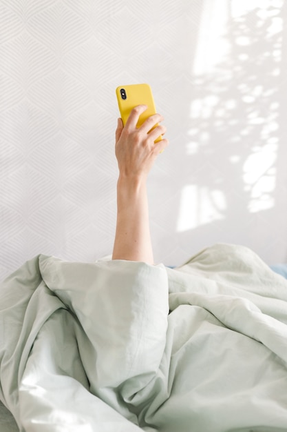 Kaukasische Frau mit Smartphone im Bett