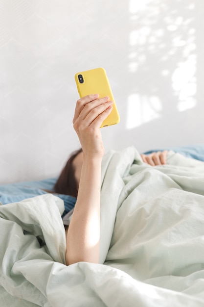 Kaukasische Frau mit Smartphone im Bett