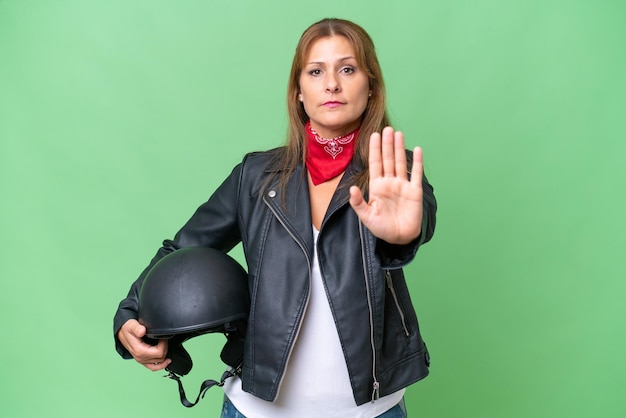 Kaukasische Frau mittleren Alters mit einem Motorradhelm vor isoliertem Hintergrund, die eine Stoppgeste macht