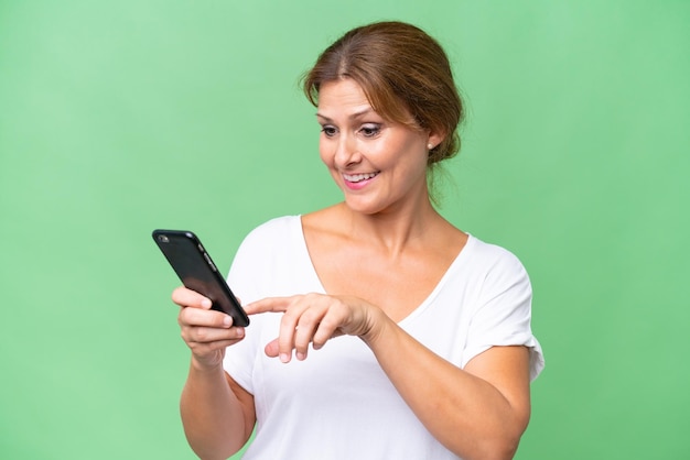 Kaukasische Frau mittleren Alters vor isoliertem Hintergrund, die eine Nachricht oder E-Mail mit dem Handy sendet