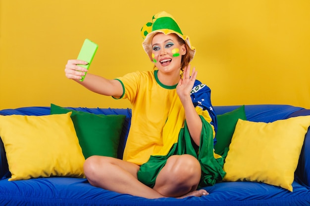 Kaukasische Frau, Rothaarige, brasilianischer Fußballfan, Brasilianerin, auf Couch bei Smartphone-Videoanruf