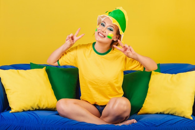 Kaukasische Frau Rothaarige Brasilien Fußballfan Brasilianer auf der Couch machen Symbol für Frieden und Liebe