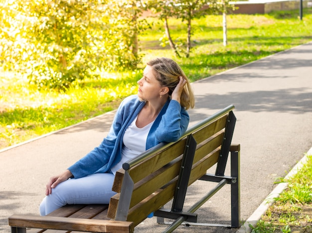 Kaukasische Frau sitzt an einem sonnigen Tag im Park auf einer Bank und bürstet ihr Haar mit der Hand