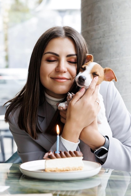 Kaukasische Frau und Jack-Russell-Terrier betrachten den Kuchen mit einer Kerze Der Hund und der Besitzer feiern den Geburtstag