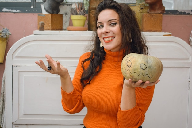 Kaukasische Frau zu Hause hält Kürbis in der Hand und zeigt ihn, dass sie Dekoration für Halloween malt