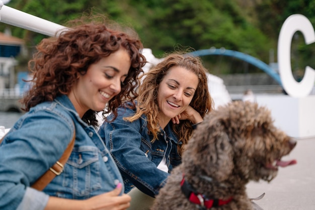 Kaukasische Frauen mit braunem Wasserhund draußen. Horizontale Ansicht von Freunden, die mit Haustier reisen. Lebensstil mit Tieren im Urlaub.