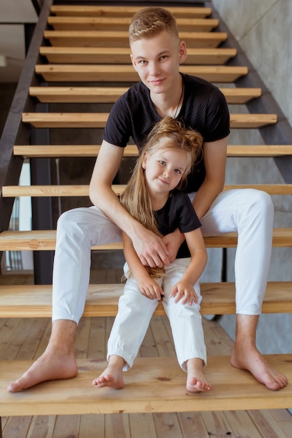 Kaukasische Geschwister Teenager Junge Bruder und kleine Mädchen Schwester sitzen auf Treppen im Loft Interieur