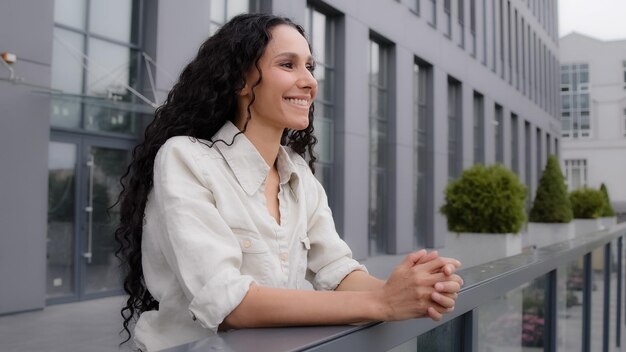 Kaukasische hispanische Frau mit gelockten langen Haaren, weibliche Geschäftsfrau steht auf der Balkonterrasse herein