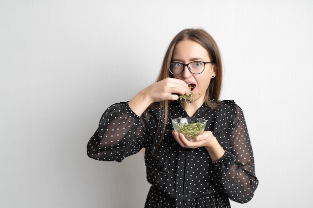 Kaukasische junge Frau mit Salat lokalisiert auf weißer Wand. Microgreens Superfood.