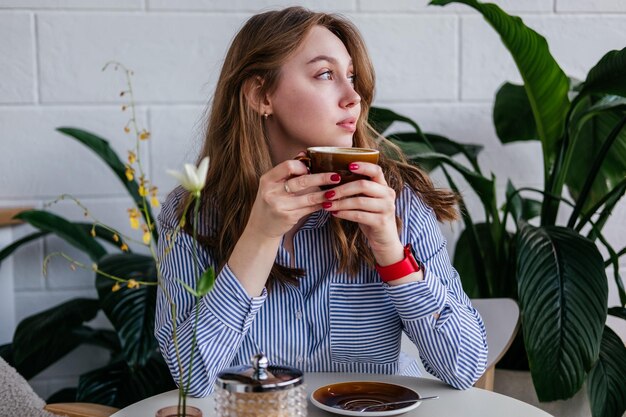 Kaukasische junge Frau sitzt im Café und schaut weg. Mädchen trinkt Kaffee im Haus.