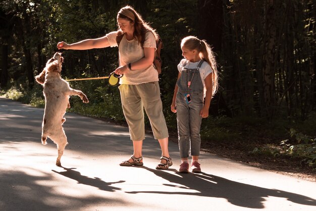 Kaukasische junge Mutter und Tochter gehen und trainieren Hund im Stadtpark