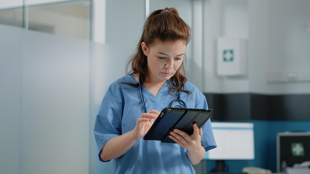 Kaukasische Krankenschwester mit digitalem Tablet mit Touchscreen für Behandlung und medizinische Versorgung. Frau, die als medizinische Assistentin arbeitet und ein modernes Gerät mit Technologie für die Gesundheitspraxis hält.