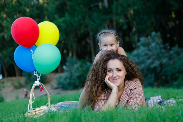 Kaukasische lächelnde Mutter und Tochter, die auf der Decke im Park sitzen. Muttertagskonzept. Glückliches Paranting-Konzept