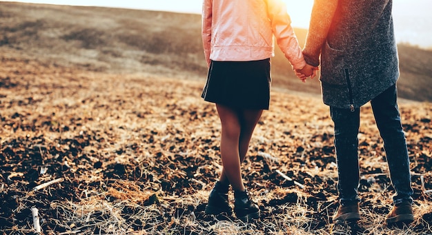 Kaukasische Liebhaber, die Hand in Hand in einem Feld während eines Herbstsonnenuntergangs aufwerfen