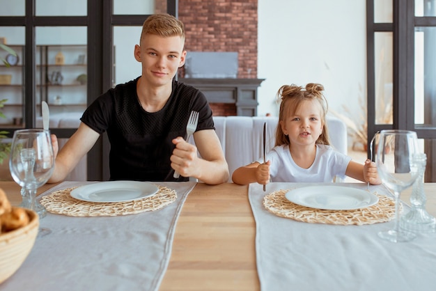 Kaukasische lustige süße Geschwister kleines Mädchen mit älterem Bruder im Esszimmer im modernen Loft-Interieur