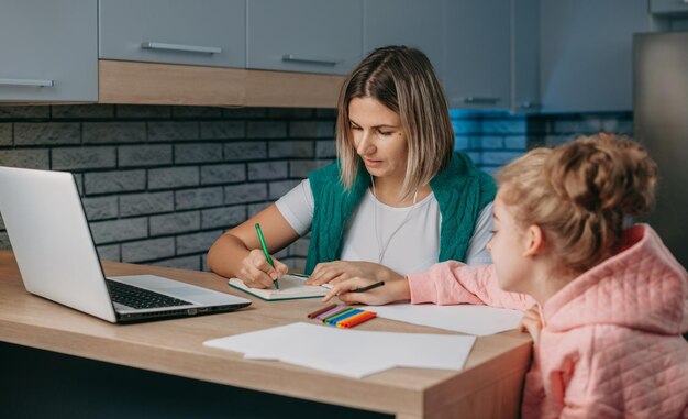 Kaukasische mutter hilft schulmädchen tochter bei der schulhausaufgabenvorbereitung kinder bildung fam...