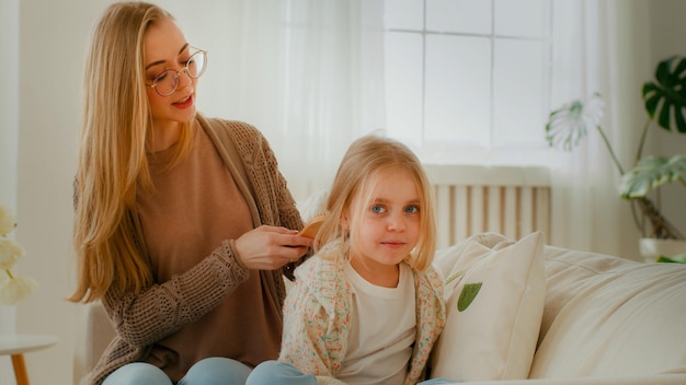 Kaukasische Mutter kämmt das Haar des niedlichen jugendlichen Mädchens, Tochter, Mutter, Babysitter, hilft kleinem Kind