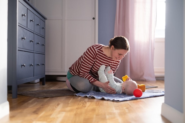 Kaukasische Mutter mit Baby macht Yoga zu Hause, um stark und gesund zu sein