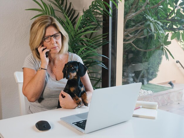 Kaukasische reife Frau, die zu Hause mit einem Computer und ihrem Dackelhund arbeitet