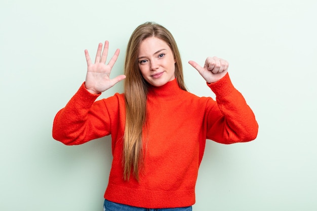 Kaukasische rothaarige Frau, die lächelt und freundlich aussieht und die Nummer sechs oder sechs zeigt, wobei die Hand nach unten zählt