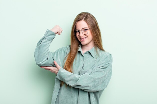 Kaukasische rothaarige Frau, die sich glücklich, zufrieden und kraftvoll fühlt, fit und muskulös Bizeps beugt und nach dem Fitnessstudio stark aussieht