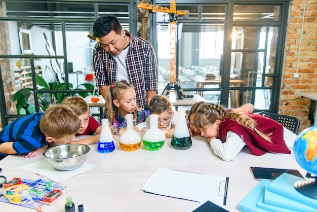 Kaukasische Schulkinder im Chemielabor. Die Schüler geben Trockeneis mit farbigen Flüssigkeiten in die Kolben, was zu einer intensiven Verdampfung führt. Wissenschaft, chemische Reaktion und Bildungskonzept.