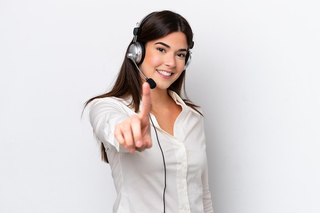 Kaukasische Telemarketer-Frau, die mit einem Headset arbeitet, das auf weißem Hintergrund isoliert ist und einen Finger zeigt und hebt