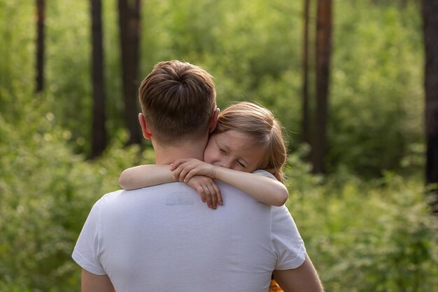 Kaukasische Tochter in den Armen von Papa und umarmt ihn mit Blick auf die Kamera im Wald. Vater und Tochter spielen zusammen, lachen und haben Spaß. Happy Family Aktivitätskonzept