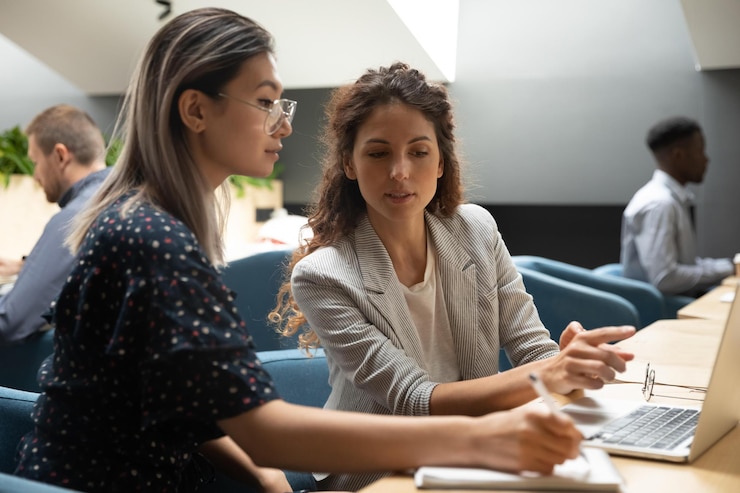 Foto kaukasische weibliche professionelle lehrerin mentor-managerin, die asiatische praktikantin anweist, erklären, dass computerprojekt-lehrarbeiter notizen machen, neue fähigkeiten bei der arbeit im bürolehrlingskurs lernen