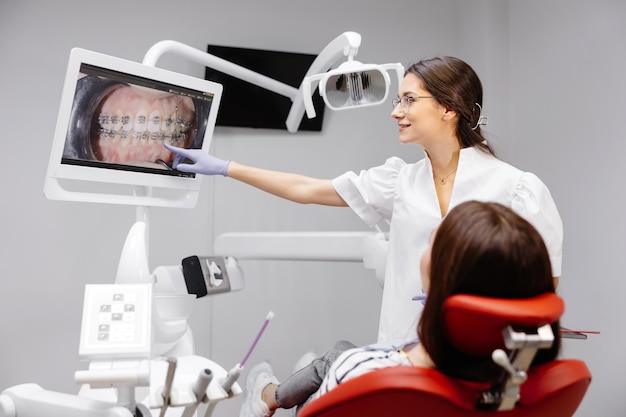 Kaukasische Zahnärztin erklärt Patientin in der Klinik Röntgenbilder auf dem Bildschirm